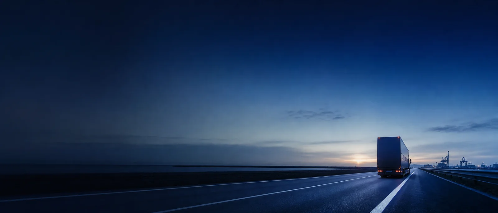 A car transporter leaves the port on a road at dawn